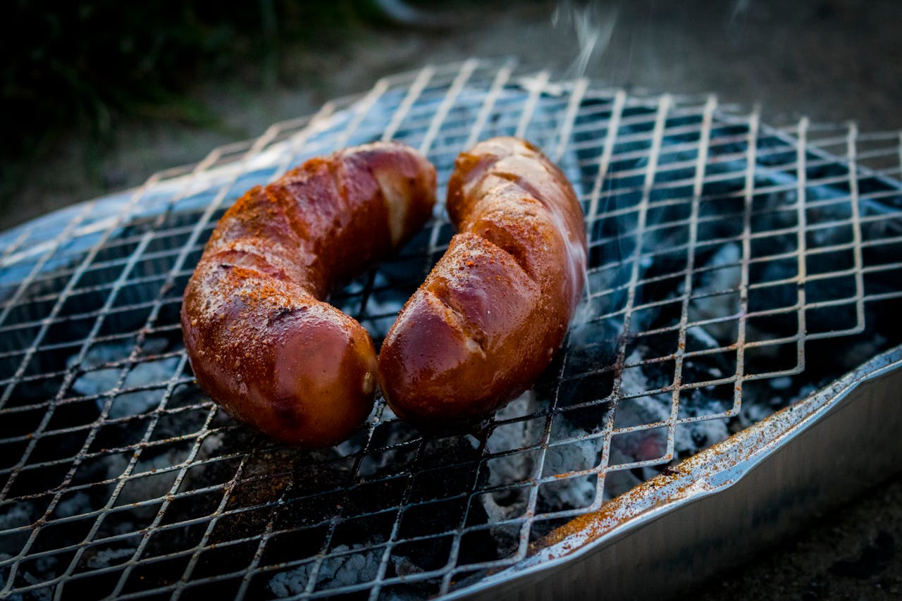 stats-img Close-up of grilled sausages on a barbecue grill with smoke rising.